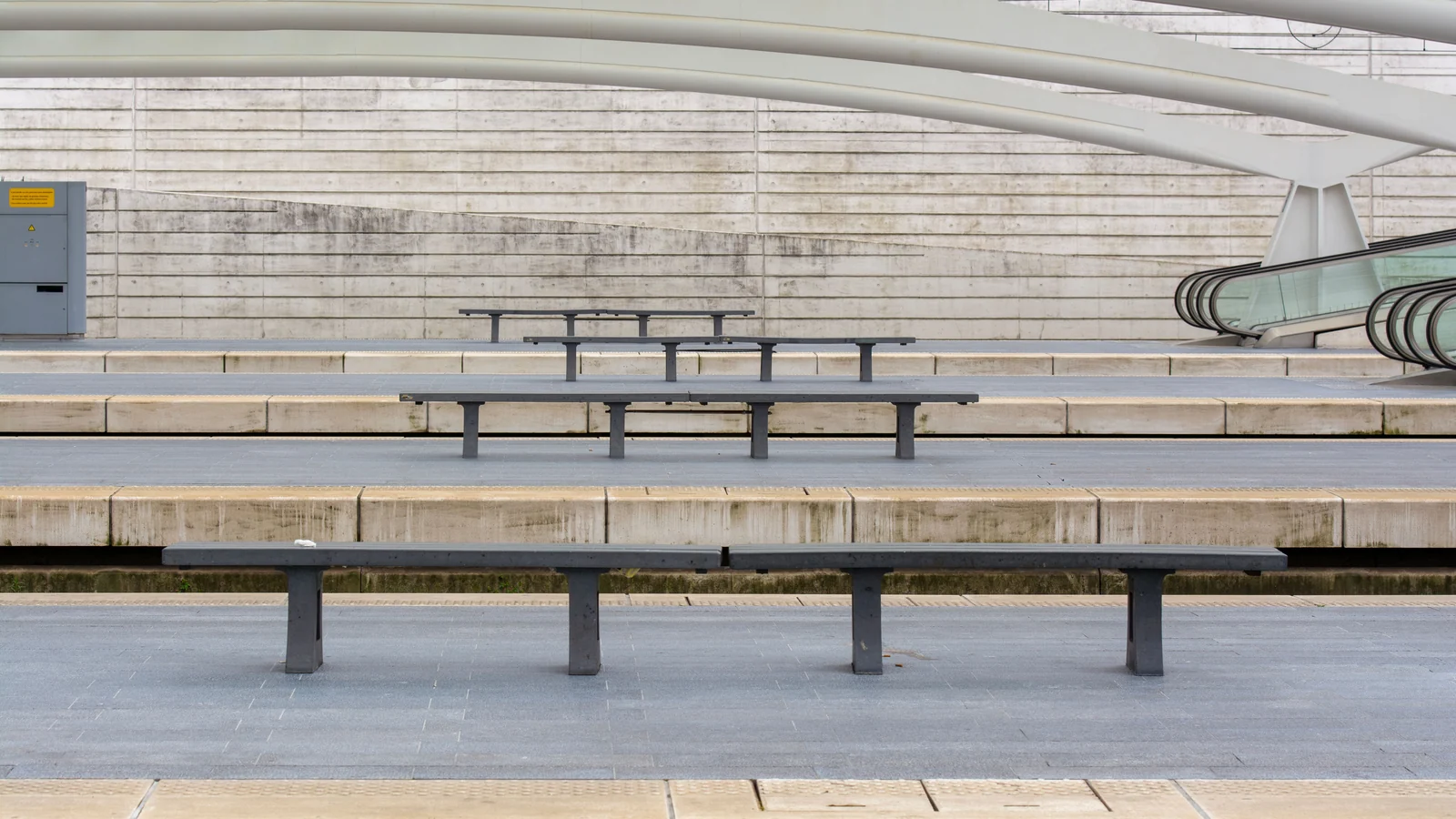 Illustrative stock image of empty platform benches beneath a curved white station roof.