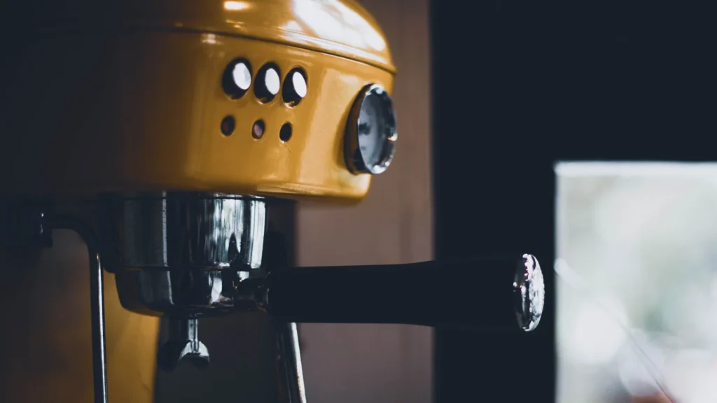 Close-up of a yellow espresso machine with a black portafilter handle.