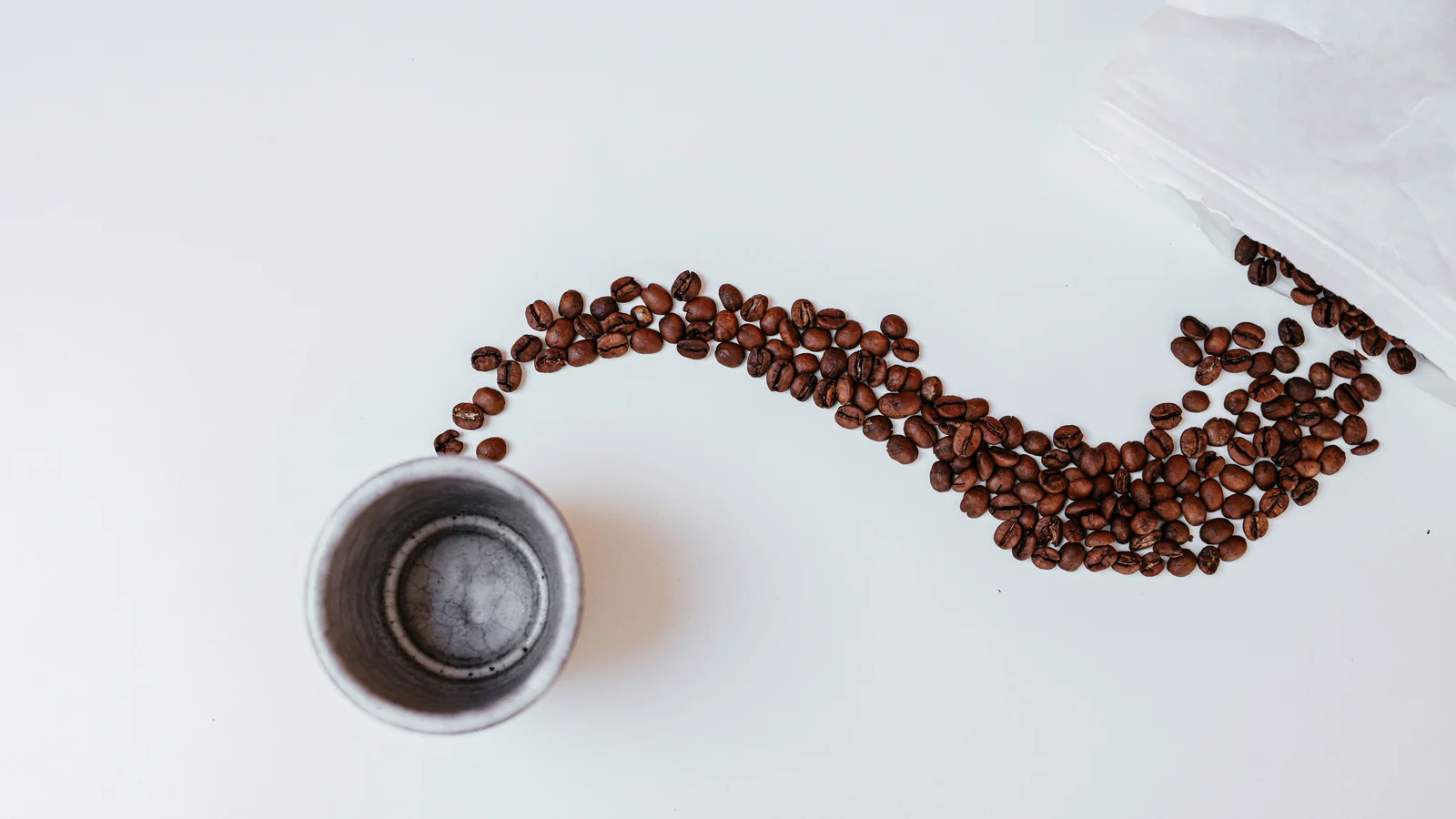 Overhead view of a small cup and coffee beans arranged across a white surface.