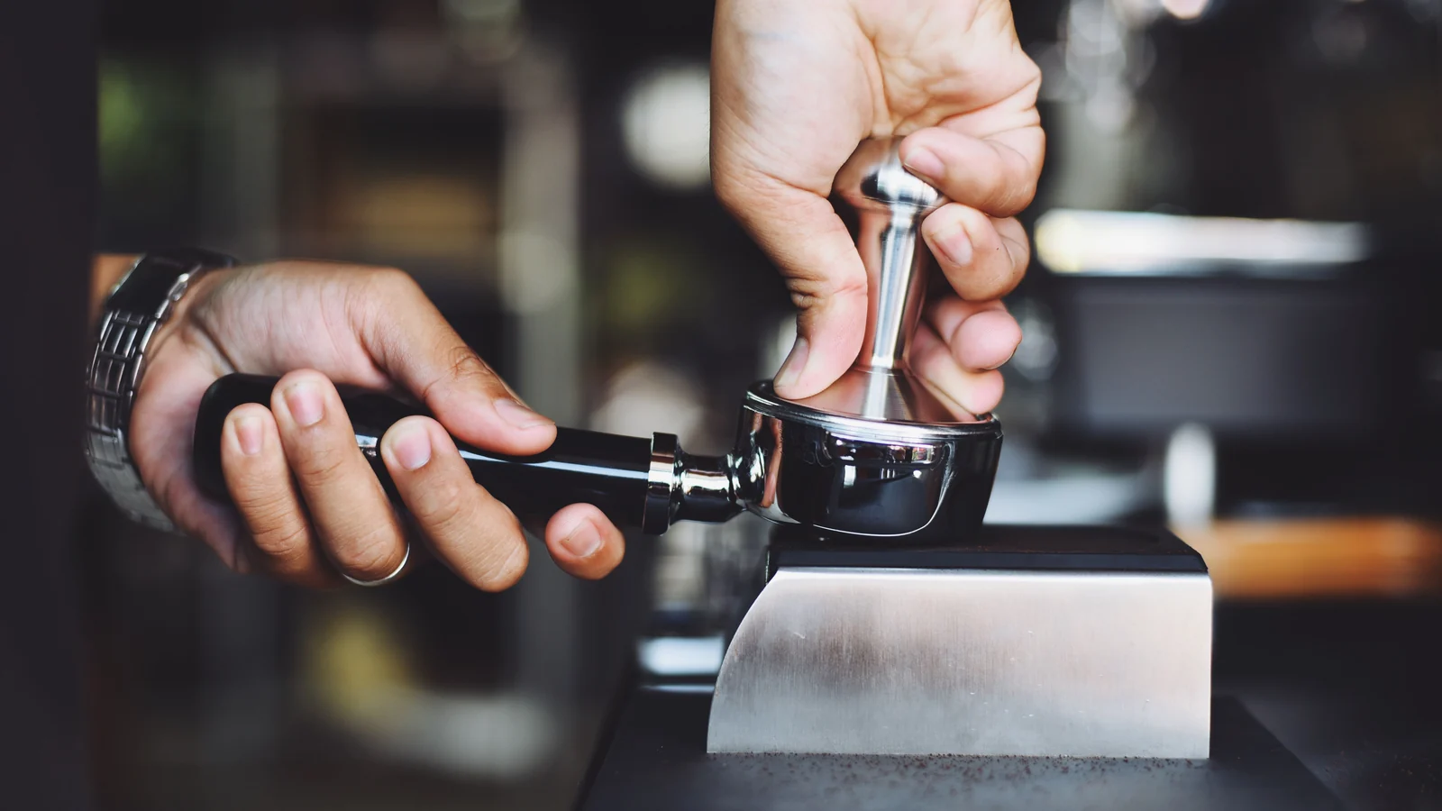 Hands pressing a tamper into a portafilter on a tamping stand.