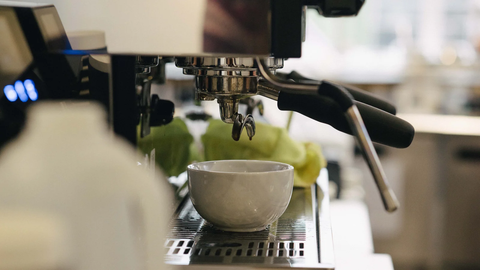A ceramic cup beneath the group head of an espresso machine, with a steam wand alongside.
